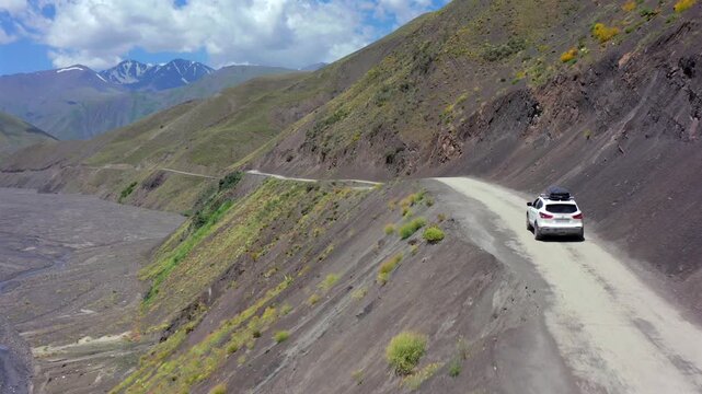 Aerial drone shot of SUV driving along narrow mountain slope road in Azerbaijan, highlighting steep hillside terrain, exposed path and remote scenic travel through rugged landscape