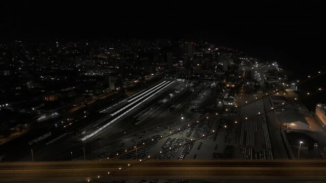 Drone flies from suspension bridge over train station at night in Maputo, Mozambique