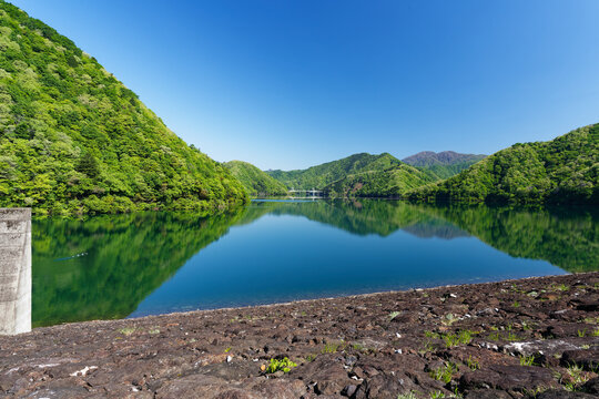 Fresh Green Mountain Lake with Reflections, Rocky Shore and Blue Sky in Spring