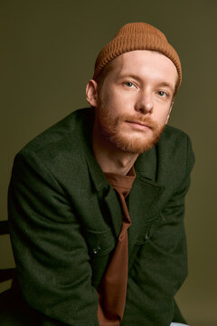 Stylish young man with a trendy hat poses confidently against a green backdrop.