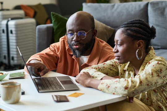 African American couple planning trip on laptop, checking booking details and travel documents at home. Useful for vacation planning, online reservation, travel budget marketing