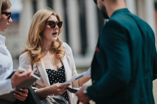 Business people review documents and talk outdoors. A small group of professionals discuss papers during an outdoor meeting.