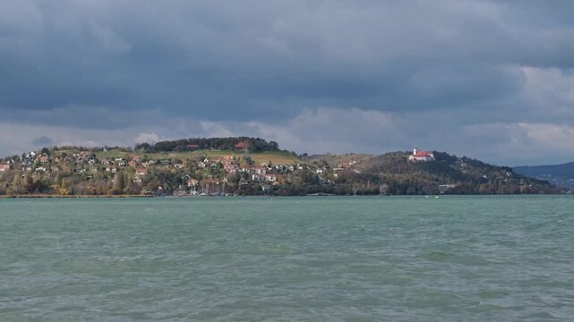 The famous Benedictine monastery and houses with amazing view on the Tihany peninsula in Hungary. Green water of Lake Balaton in the foreground. Autumn landscape with sunshine and dark blue clouds.