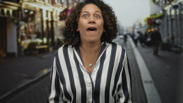 Woman covers mouth with both hands on busy city street with blurred shoppers and buildings in view; shock wonder awe surprise.