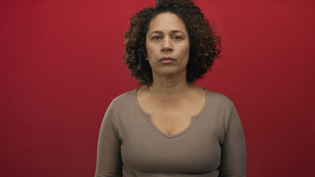 Woman middle age hispanic with visible cleavage and subtle expression against red studio wall; contemplation.