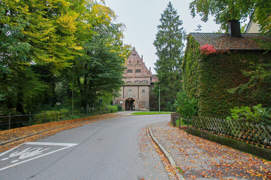 Historic Kempter Tor brick gate in Memmingen, Bavaria, Germany. Autumn landscape with colorful yellow trees, fallen leaves on the road and old architecture.
