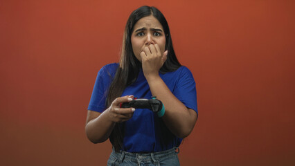 Young woman gamer biting her fingernails while holding a gamepad in studio with worried expression and tense posture  nervous anticipation. © Krakenimages.com