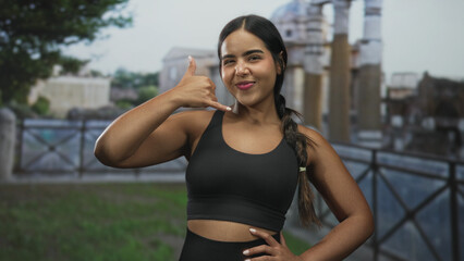 Fototapeta premium Woman showing call hand gesture and smiling at camera in historic building; confidence motivation wellness.