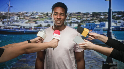 Naklejka premium Man answering questions to reporters with microphones and smartphone at harbor pier, boats and town behind him; confidence public statement.
