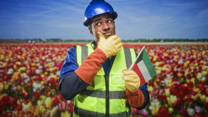 Naklejka premium Man holding kuwait flag and pointing index finger up in tulip field, wearing hardhat and safety vest; pride celebration.