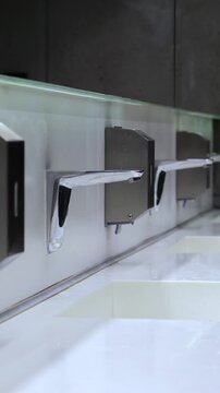 Modern public restroom with white ceramic sinks in a row, featuring automatic chrome faucets and integrated soap dispensers for a touchless, hygienic handwashing experience