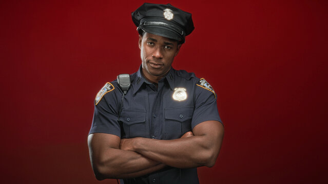 Black man police officer with forearms crossed, badge and radio visible in studio; authority seriousness.