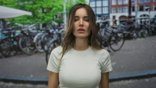 Young hispanic woman in white t-shirt flips middle fingers with bare hands on city street; anger defiance.
