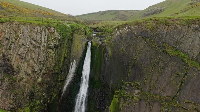 Aerial view of surroundings at Spekes Mill Mouth waterfall which is  located in a beautiful coast area of rugged valleys, high cliffs and wildflowers flourish. Drone POV of United Kingdom landscapes. 