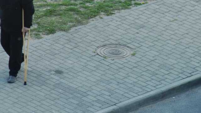 A man with a broken leg walks on crutches along the sidewalk, copy space for text