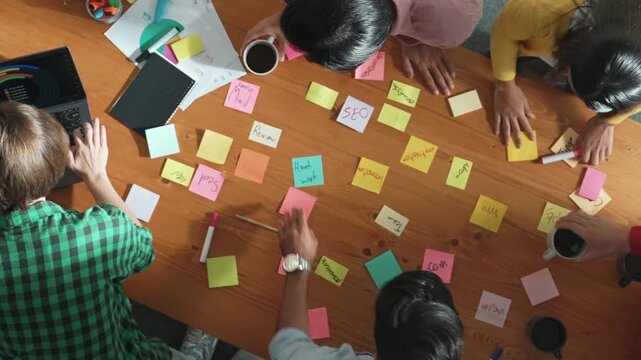 Top down aerial view of business people putting sticky note on whiteboard. Group of diverse people working together choosing brainstorming creative idea and placed on board at meeting. Convocation.