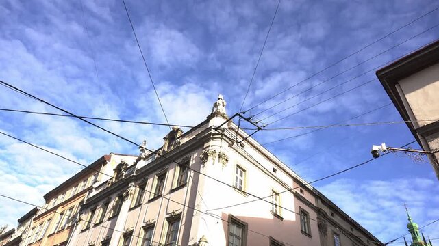 Low perspective view of classical European architecture, decorative details of old buildings against bright blue sky and white clouds, intricate web of power cables above, sunny day city street