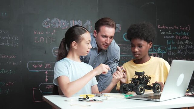 Caucasian teacher pointing at laptop screen while explain car model system at blackboard with coding or programming code written. Happy diverse student learning about robotic construction. Edification