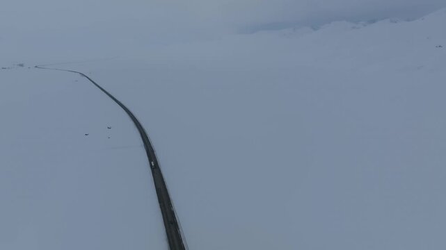 Drone footage of a lonely asphalt road cutting through vast snowfields at Ala-Bel Pass, high in the Tien Shan mountains of Kyrgyzstan, cold winter landscape