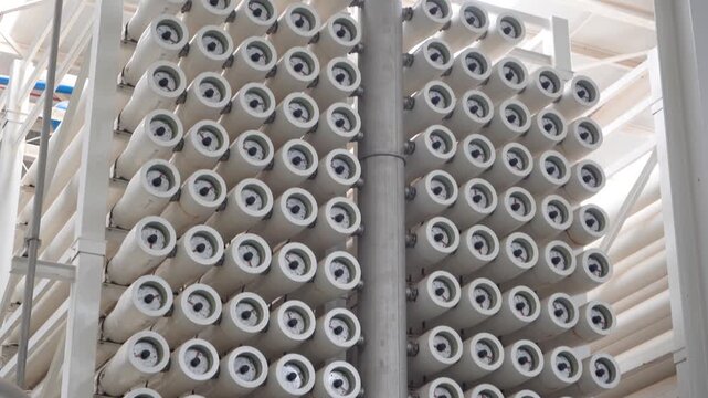 Tilt-down shot of massive stacks of white reverse osmosis membrane filters inside a modern water desalination plant. Perfect for content on water treatment, sustainability, and clean infrastructure.