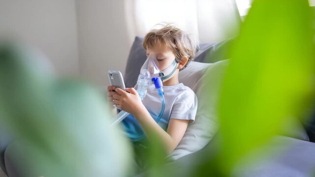 Child using smartphone while wearing nebulizer mask at home, pediatric respiratory treatment concept with inhalation therapy, asthma care, illness recovery and modern digital lifes
