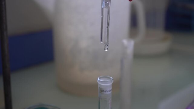 Extreme close-up of clear liquid slowly dripping from a glass burette into a test tube in a lab. Perfect macro B-roll for chemistry, titration, scientific precision, and pharmaceutical research.
