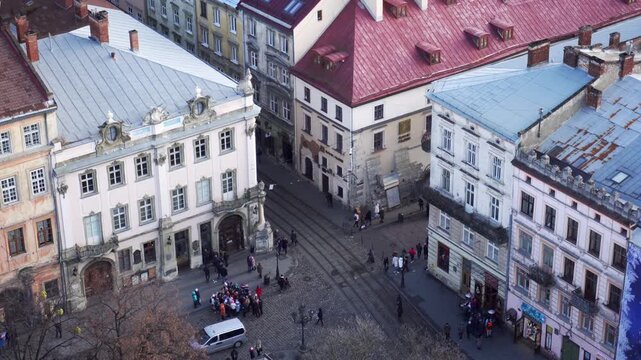 High angle view captures bustling urban landscape featuring old European style buildings, diverse roof colors, people walking on paved street with tram lines, light traffic of one vehicle