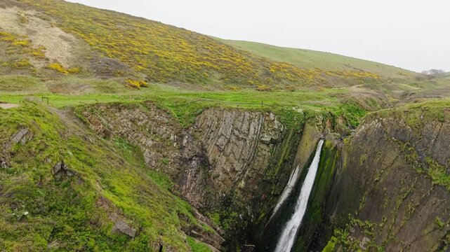 Aerial view of surroundings at Spekes Mill Mouth waterfall which is  located in a beautiful coast area of rugged valleys, high cliffs and wildflowers flourish. Drone POV of United Kingdom landscapes. 