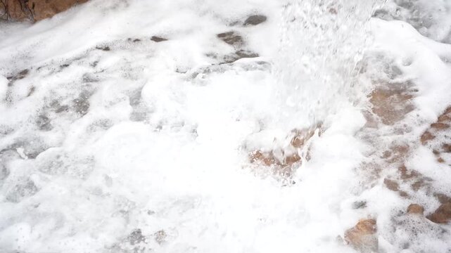 Close-up of a powerful water stream crashing into a muddy pool, creating thick white foam and churning turbulence. Ideal dynamic B-roll for flooding, irrigation, and industrial water extraction.