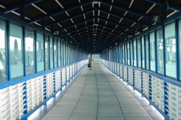 A solitary person walking down a long enclosed pedestrian bridge. © NFS Studio