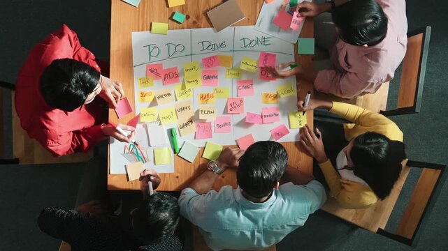 Top view of people writing and making scrum task board while writing marketing and planning strategy at colorful sticky notes. Smart team manage work performance by using kanaban board. Convocation.