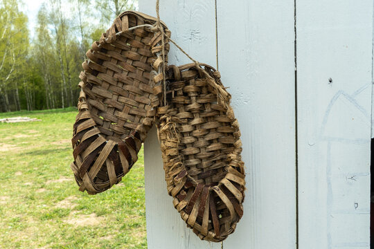 Traditional russian bast shoes hanging on a white wooden fence outdoors. Handmade antique wicker footwear from tree bark as symbol of rural life and ancient slavic culture