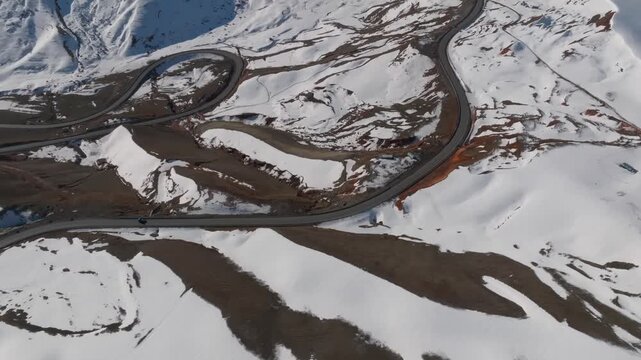 Drone footage of a serpentine asphalt road crossing snowy mountains at Chyyyrchyk Pass. Winter landscape with switchbacks, ridges, and patches of bare ground