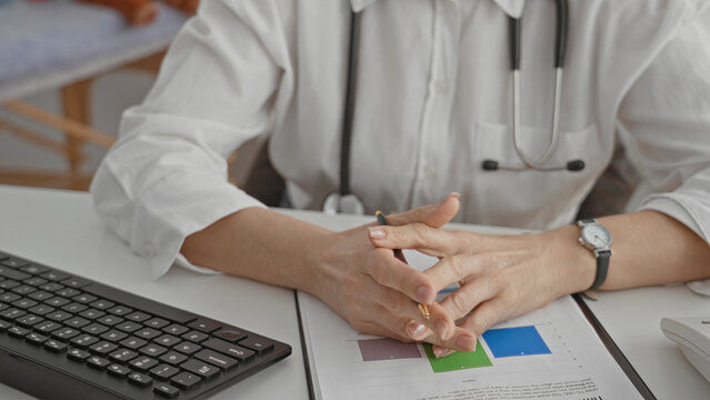 Hispanic woman doctor gesturing with hands over medical report holding pen and visible stethoscope on chest in clinic building; professional reassurance.