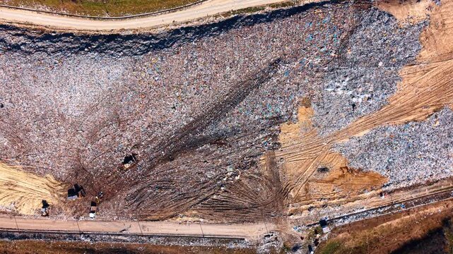 Trash heaps at waste site. Dump trucks move through a landfill covered with various types of waste during daylight hours near a road.