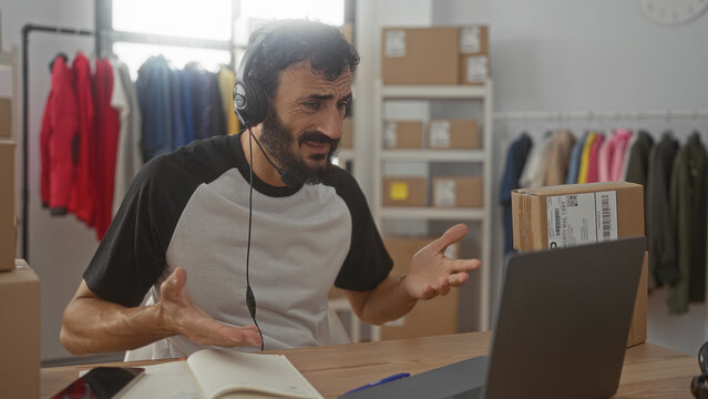 Man with headset raises hands beside laptop and shipping box in packing studio; frustration customer support.