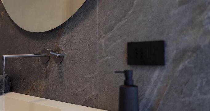 Contemporary bathroom interior with large round mirror wall faucet and integrated sink, slow right to left camera move reveals dark large format stone look tiles light countertop and wooden vanity