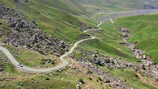 Aerial drone shot, winding serpentine mountain road crossing green hills in Azerbaijan, highlighting curved path geometry, natural terrain patterns, scenic highland landscape minimal vehicle presence 