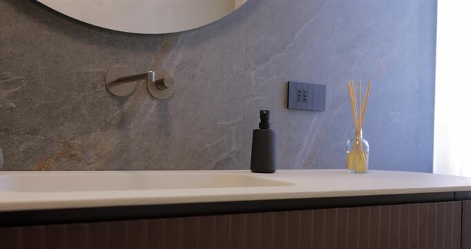 Contemporary bathroom vanity with ribbed natural wood and pale stone countertop, smooth camera glide follows curved cabinet beneath round mirror and built in wall faucet against dark stone