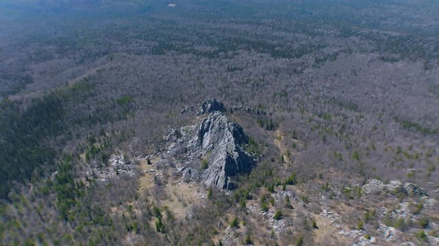 Drone footage flying above a jagged rocky ridge surrounded by taiga forest in Taganay National Park near Zlatoust, Chelyabinsk Oblast, Russia on a clear day
