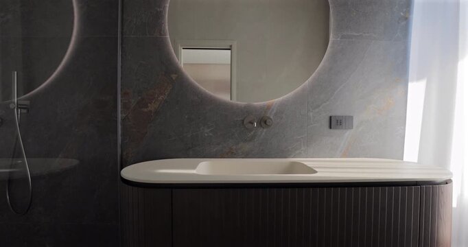 Designer bathroom vanity with glass shower and large round mirror, static video of fluted wood cabinetry integrated sink wall mounted faucet and dark stone wall lit by soft daylight