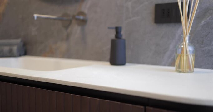 Luxury wooden vanity and integrated sink in modern bathroom interior, slow camera glide follows curved cabinet beneath light countertop while dark natural stone wall and minimalist faucet shape