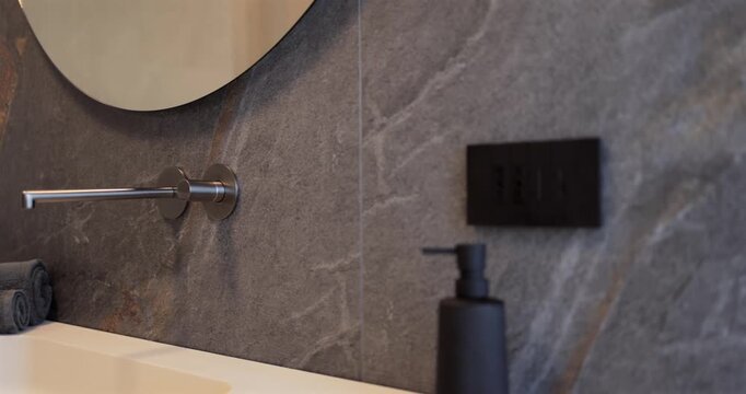Modern bathroom interior with monolithic sink wood vanity and rounded mirror, slow camera pan reveals wall mounted faucet dark stone surfaces light countertop and soft daylight across a washroom