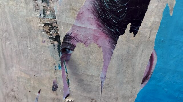 Close up video of a torn old poster peel from a weathered wall fluttering in the wind, creating an urban textured abstract background