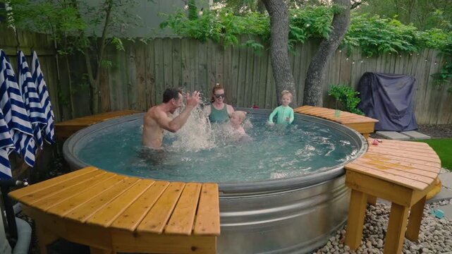 Family of four splashing big in a backyard stocktank pool with water flying, slow motion summer vacation in 4k. Family lifestyle ads, summer fun content, and pool day commercials.