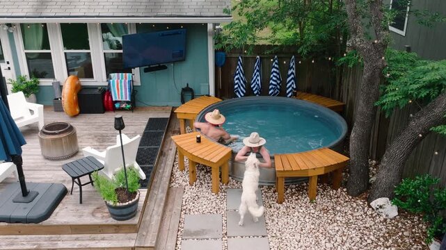 Couple relaxing in a backyard hot tub with sun hats petting dog, watching golf. Outdoor luxury lifestyle, dream home summer content