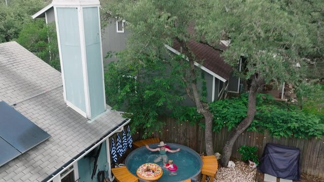 Aerial close drone shot of a mom and her kids floating with a donut tube in a backyard stocktank pool. Family lifestyle, summer fun, and pool day content.