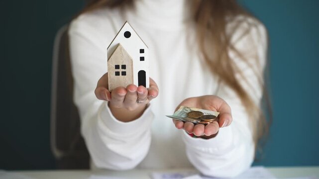 Woman holding cash in one hand and a miniature house in the other, illustrating financial planning, saving money, and budgeting for buying a new home or property investment.