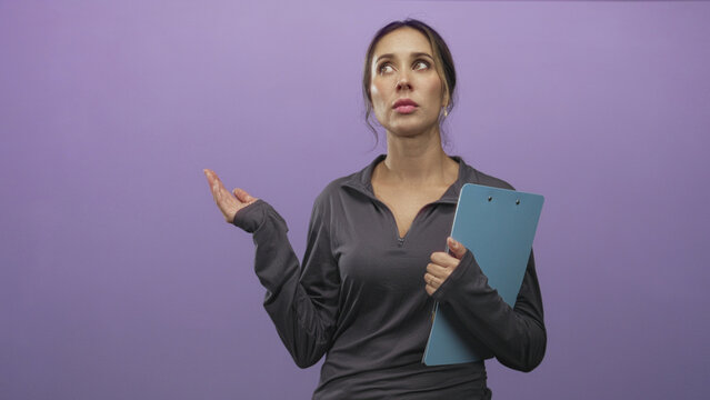 Woman holding blue clipboard with hand to chest and shrug gesture in studio; exasperation coaching instruction.