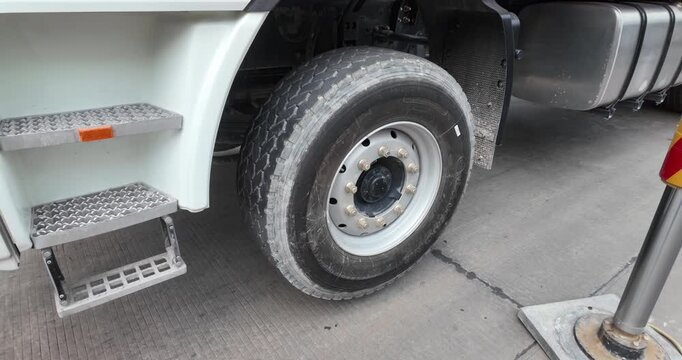 Tilt up view of a white cement mixer truck's elevated wheel moving as the drum rotates.